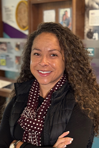 Headshot of Bailey Williams, smiling, wearing a maroon scarf with white polka dots and a black shirt and puffer vest