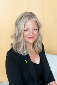 Headshot of Jami Gleason, smiling, wearing a black shirt and black blazer