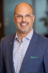 A professional headshot of a man wearing a blue suit.