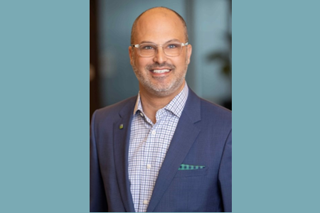 A professional headshot of a man in a blue suit.