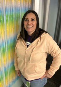 A woman smiling at the camera leaning against a decorated wall.